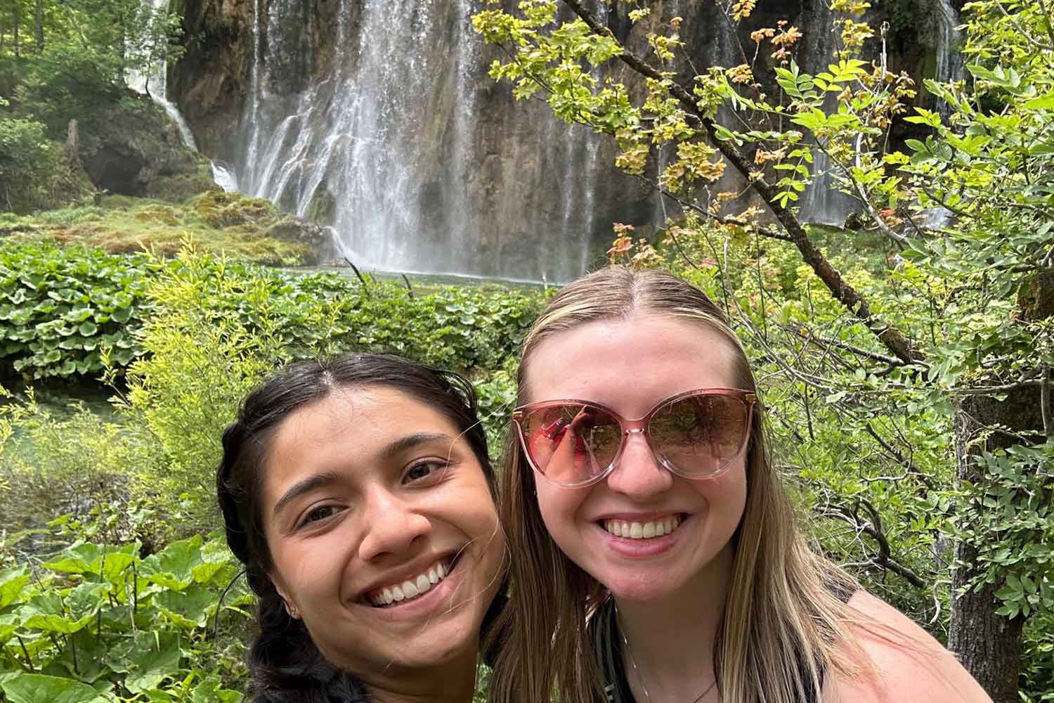 Two students in front of a waterfall in the jungle