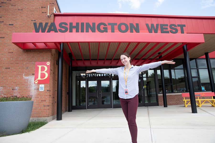 Graduate in front of sign for Washington West school