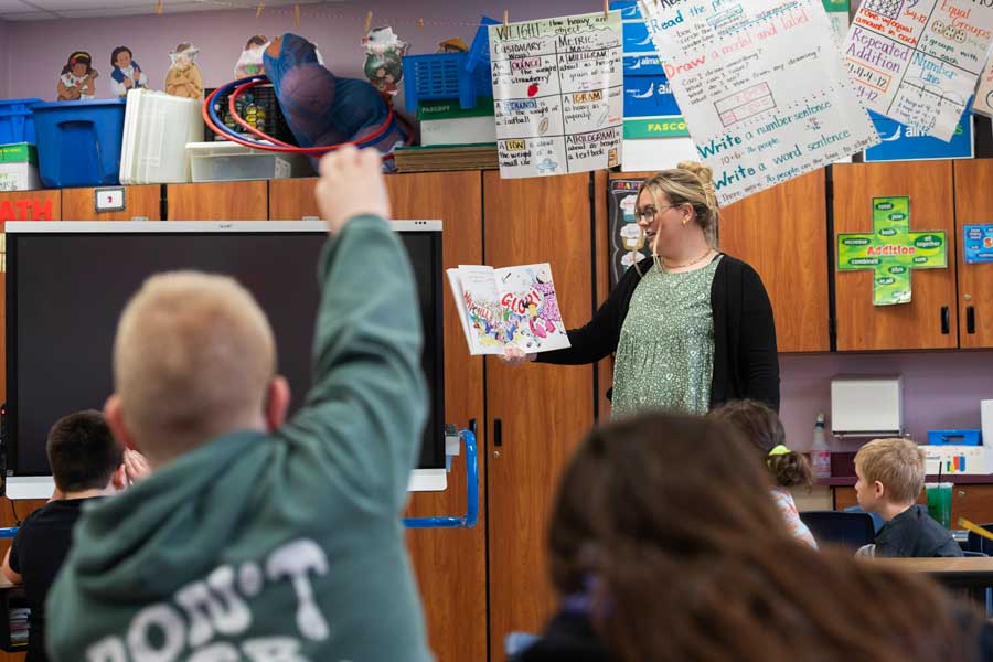 Student Teacher in classroom with children raising their hands